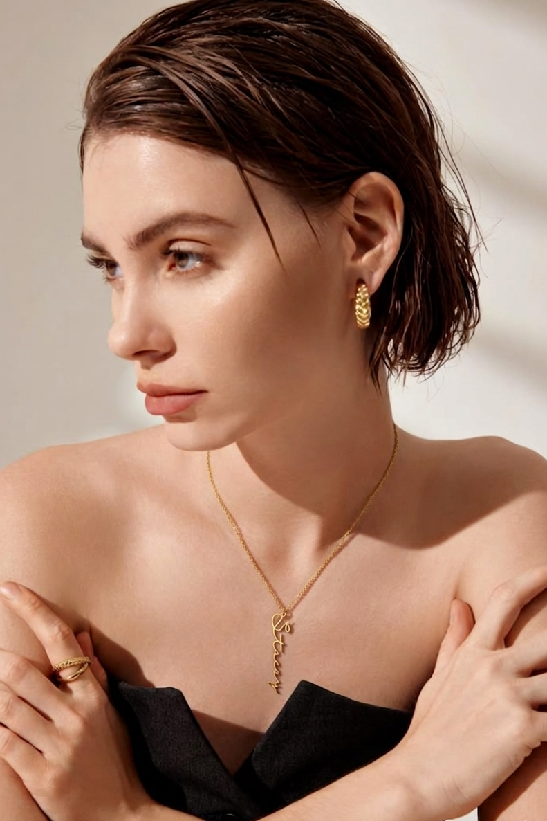 Woman wearing a gold personalized vertical name necklace with matching earrings and rings in a minimal luxury style.